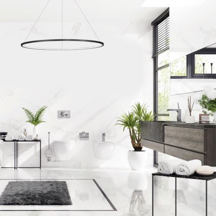 Moderná kúpeľňa s bielym mramorovým obkladom. V priestore sa nachádza toaleta, bidet, umývadlo a nábytok z tmavého dreva. Svetlo dopadá z veľkého okna s žalúziami. Na podlahe je šedý koberec.