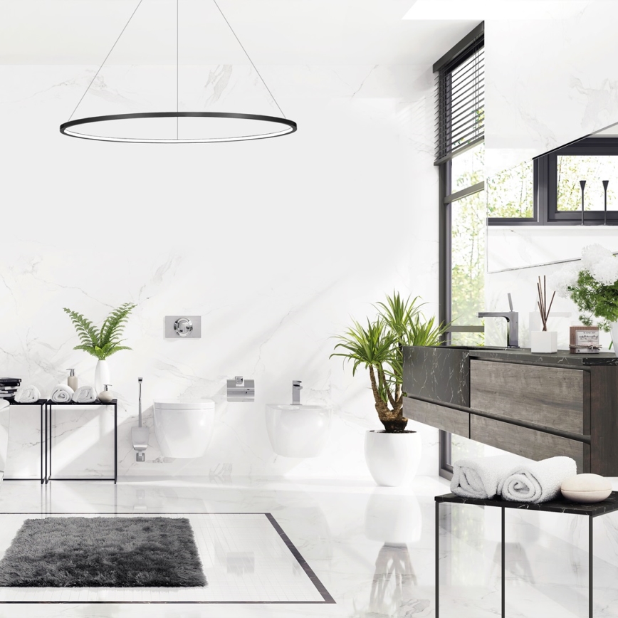 Moderná kúpeľňa s bielym mramorovým obkladom. V priestore sa nachádza toaleta, bidet, umývadlo a nábytok z tmavého dreva. Svetlo dopadá z veľkého okna s žalúziami. Na podlahe je šedý koberec.