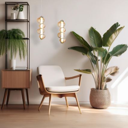 Dve zavesené svietidlá s guľovitými sklenenými prvkami visia na stene. V miestnosti sa nachádza drevené kreslo s bielym čalúnením, rastlina v kvetináči a drevená polička.