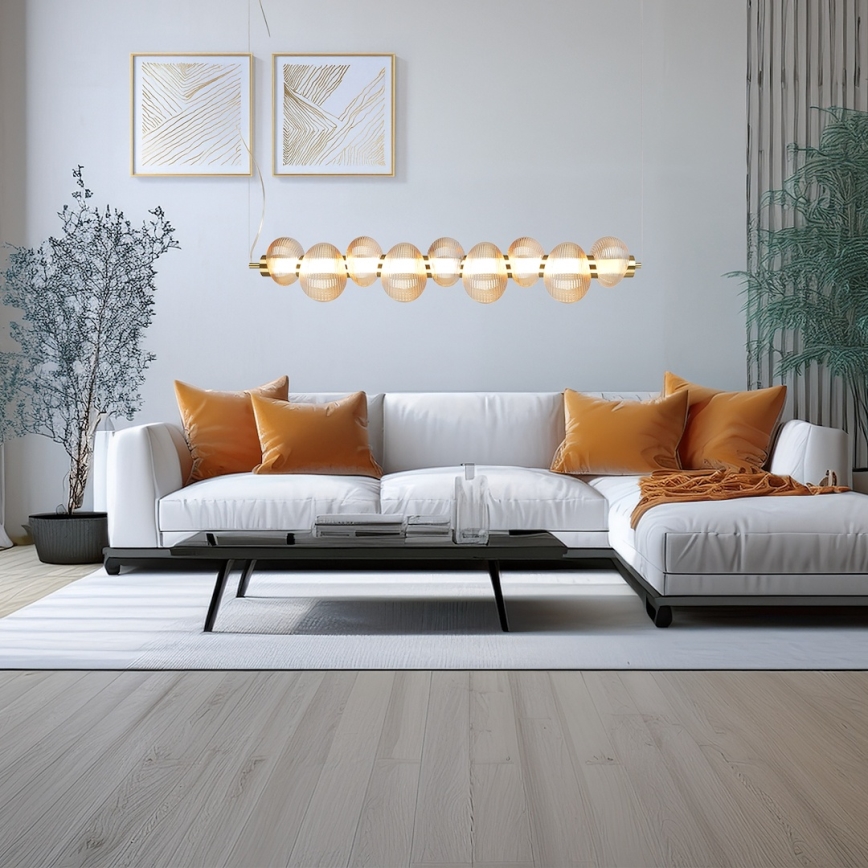 Dlhá stropná lampa s guľôčkami zo skla visí nad bielou rohovou sedačkou. Sedačka je doplnená oranžovými vankúšmi. Miestnosť je zariadená moderným nábytkom a svetlými stenami.