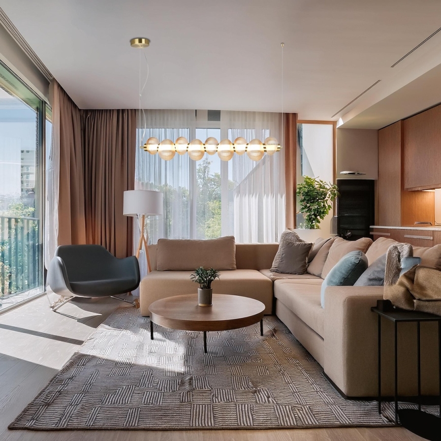 Dlhá stropná lampa s guľôčkovými tienidlami visí nad rohovou sedačkou v moderne zariadenej obývačke s oknami a kobercom.