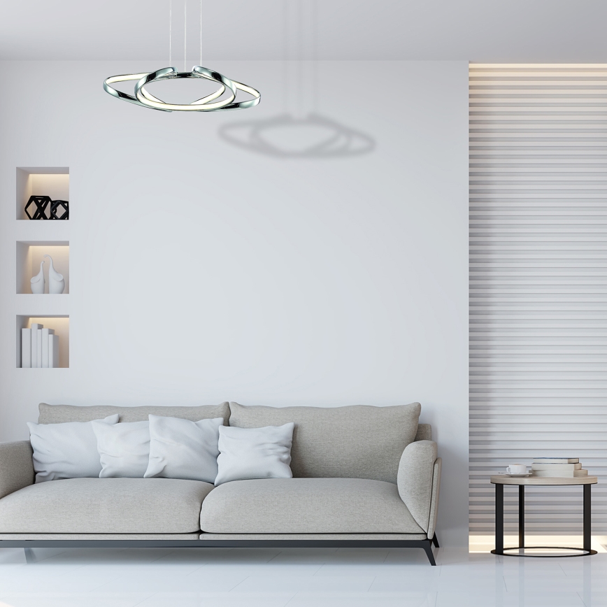 Biela sedačka s tmavými vankúšmi stojí pred stenou so štruktúrovaným povrchom. Nad sedačkou visí moderné stropné svietidlo s troma prepletenými kruhmi.