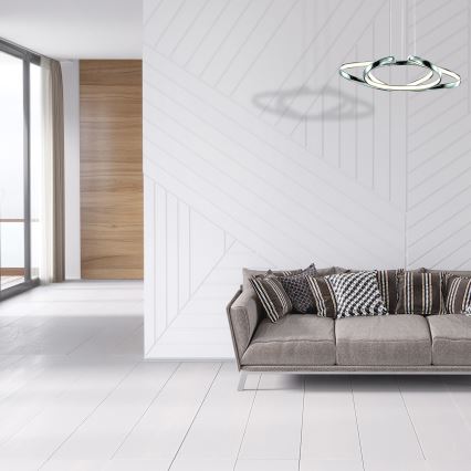 Svietidlo s dvoma prekrývajúcimi sa kruhmi visí nad bielou pohovkou v svetlej miestnosti s drevenou podlahou a nízkym dreveným stolíkom.