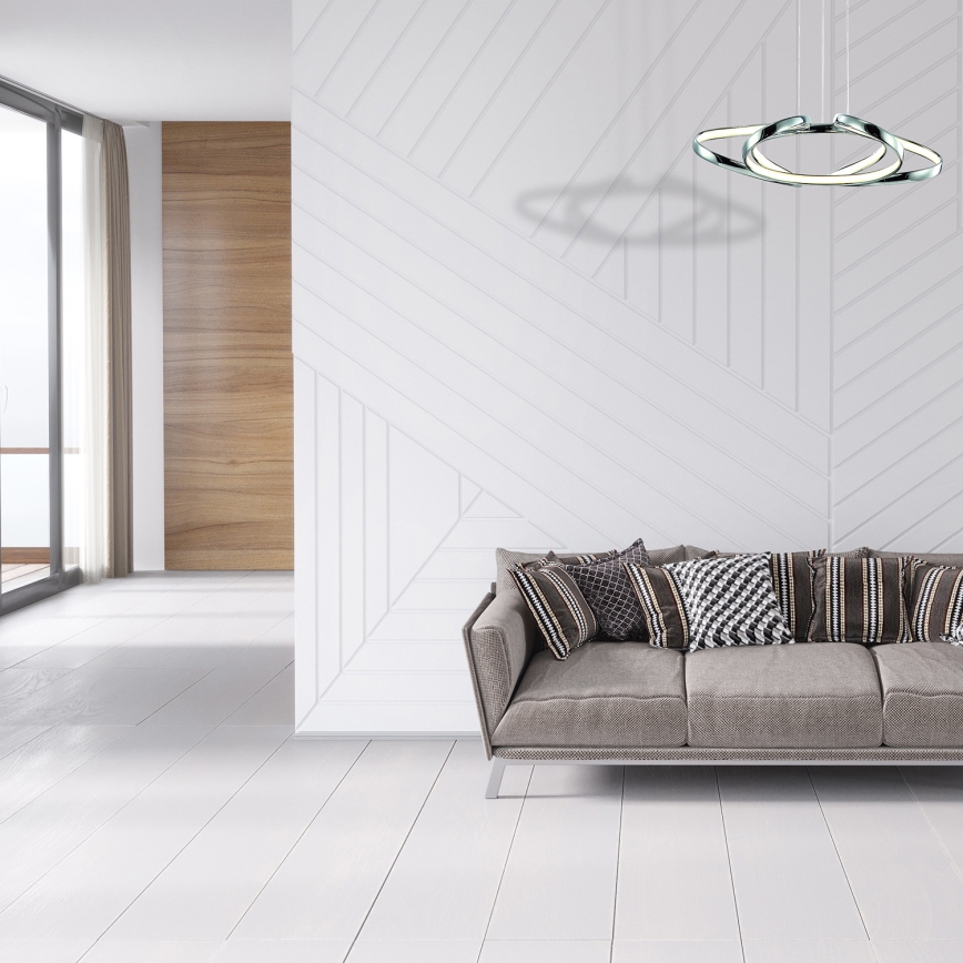 Svietidlo s dvoma prekrývajúcimi sa kruhmi visí nad bielou pohovkou v svetlej miestnosti s drevenou podlahou a nízkym dreveným stolíkom.