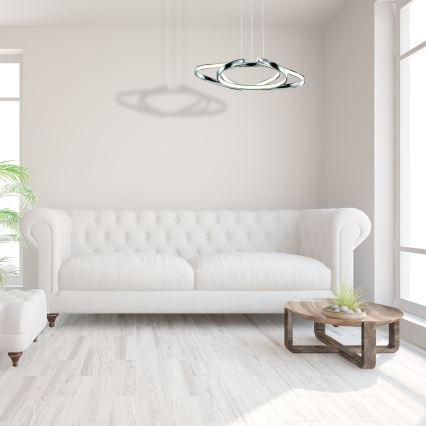 Závesné svietidlo s dvoma prepletenými kovovými kruhmi, ktoré obsahujú LED osvetlenie, visí zo stropu.