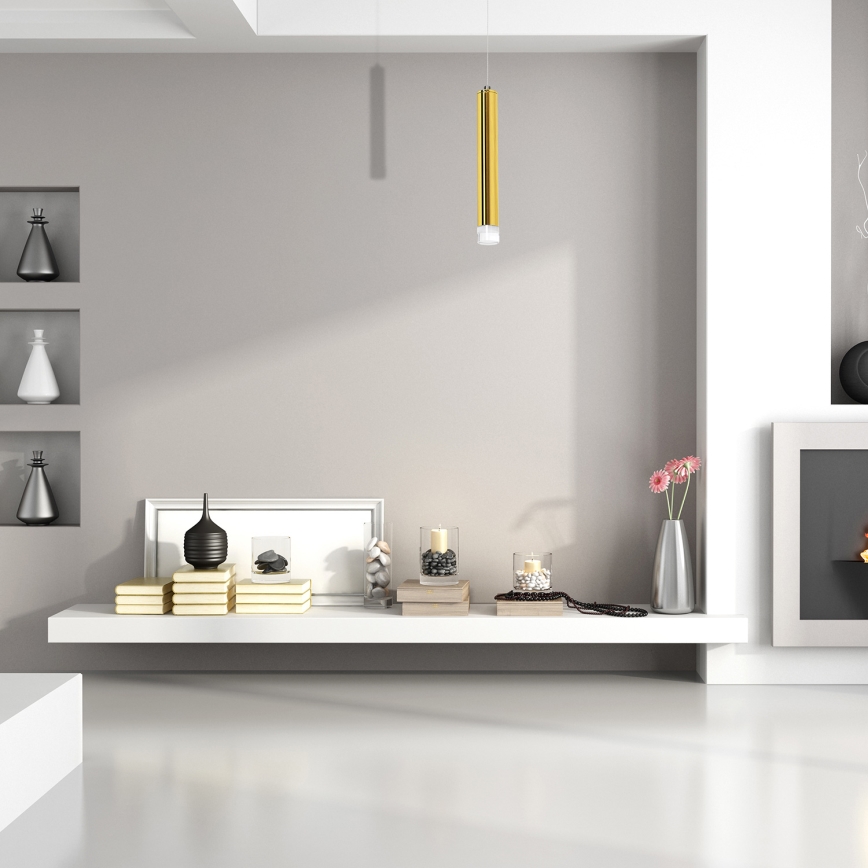 Zlatý valcový závesný svietidlo visí na tenkom kábli. Spodná časť svietidla je ukončená priesvitným valčekom. Biele pozadie.