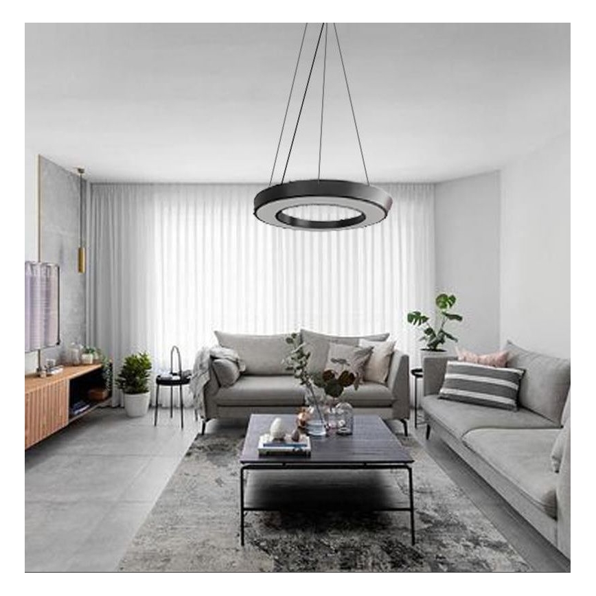 Kruhové stropné svietidlo visí v obývacej izbe. Svietidlo je čierne s vnútorným bielym kruhom. Izba obsahuje sivú sedačku, konferenčný stolík a koberec.