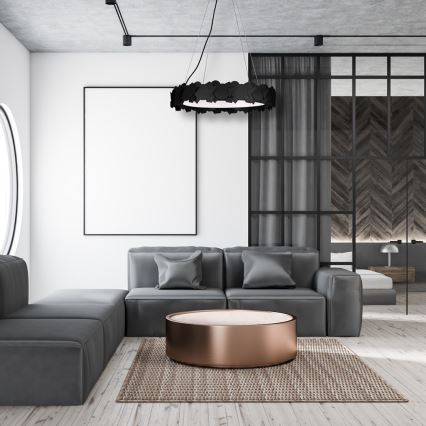 Svietidlo svieti v obývacej izbe. Moderná sedačka s nízkym konferenčným stolíkom a kobercom sa nachádza v miestnosti s bielymi stenami, drevenou podlahou a tmavými dverami.