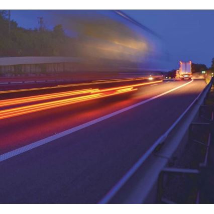 Kamión jazdí po diaľnici v noci. Svetlá vozidiel vytvárajú svetelné stopy. V pozadí je tmavá krajina.