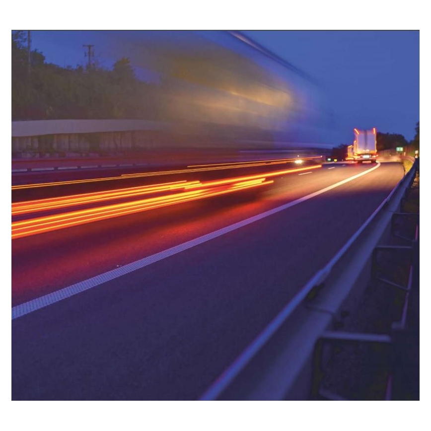 Kamión jazdí po diaľnici v noci. Svetlá vozidiel vytvárajú svetelné stopy. V pozadí je tmavá krajina.