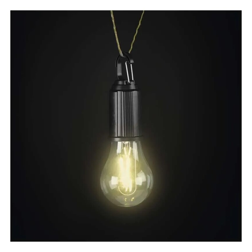 Žiarovka svieti. Je zavesená na šnúrke na tmavofialovom pozadí. Žiarovka má čierny kovový kryt.