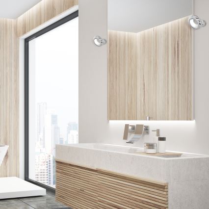 Dve nástenné svietidlá osvetľujú umývadlo s drevenou skrinkou v modernej kúpeľni s výhľadom na mesto.