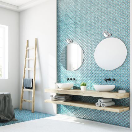 Dva umývadlá sú umiestnené na drevenej vaničke s policami v kúpeľni. Nad umývadlami visia okrúhle zrkadlá s nástennými svietidlami. Stena je obložená svetlomodrými mozaikami.