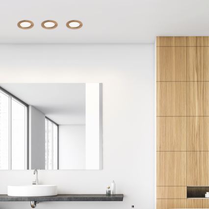 Tri kruhové svietidlá sú osadené na bielom strope kúpeľne. Pod nimi je umývadlo s batériou a zrkadlo na stene. Vedľa je drevená stena.