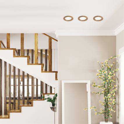 Drevené schodisko vedie nahor v interiéri domu. Na strope sú tri okrúhle svietidlá. V pozadí je vidieť časť jedálne.