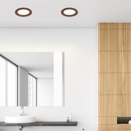 Dve kruhové svietidlá s dreveným rámom sú osadené na bielom strope. Nachádzajú sa v kúpeľni s bielymi stenami, drevenou stenou, umývadlom a zrkadlom.