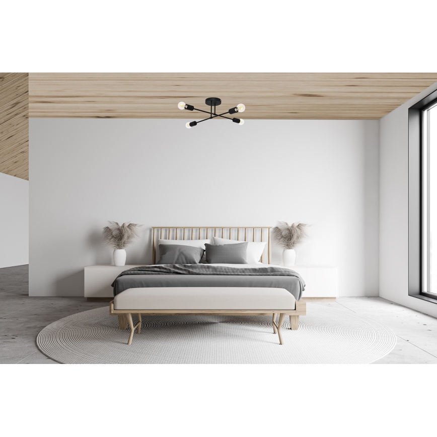 Stropné svietidlo s piatimi ramenami a žiarovkami je umiestnené v spálni. Svietidlo je čierne, svieti v minimalistickej spálni s drevenou posteľou a svetlým nábytkom.