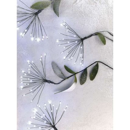 Svetlá vo forme vetvičiek s mnohými malými LED diódami sú umiestnené na svetlomodrom pozadí s umelými zelenými listami.