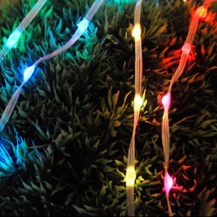 Svetlené LED pásky s farebnými diódami sú položené na umelej tráve. Diódy svietia v červenej, modrej, zelenej a žltej farbe.