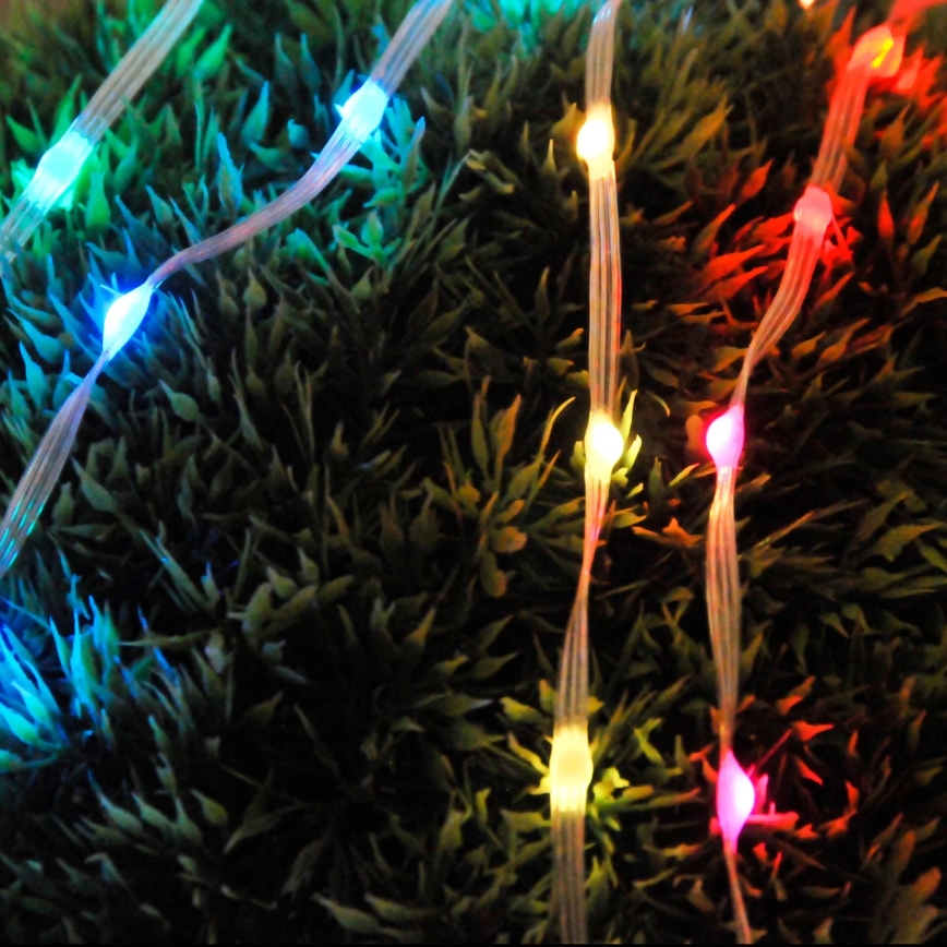 Svetlené LED pásky s farebnými diódami sú položené na umelej tráve. Diódy svietia v červenej, modrej, zelenej a žltej farbe.