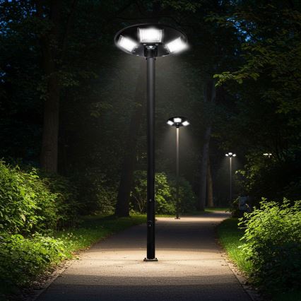 Lampáš s viacerými svetlami svieti v noci na chodníku lemovanom zeleňou. Chodník vedie parkom medzi stromami. V pozadí sú ďalšie lampáše.