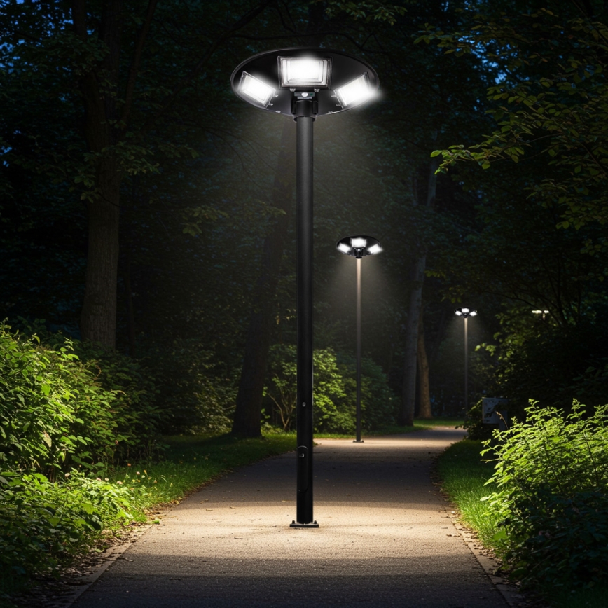 Lampáš s viacerými svetlami svieti v noci na chodníku lemovanom zeleňou. Chodník vedie parkom medzi stromami. V pozadí sú ďalšie lampáše.