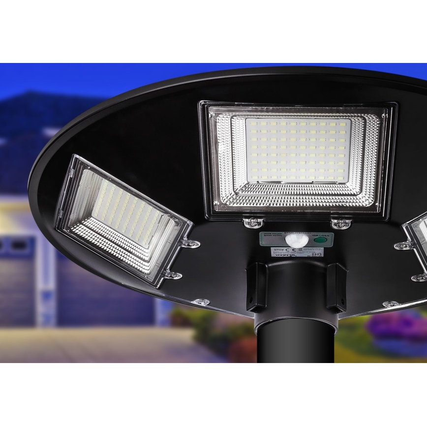 Solárny svietiaci stĺpik s tromi LED panelmi svieti. Je namontovaný na čiernom stĺpe. Pozadí tvorí rozmazané prostredie dvora. Na svietidle je vidieť nápisy: smart sensor, ON/OFF, WOTTA, CE a 50W.