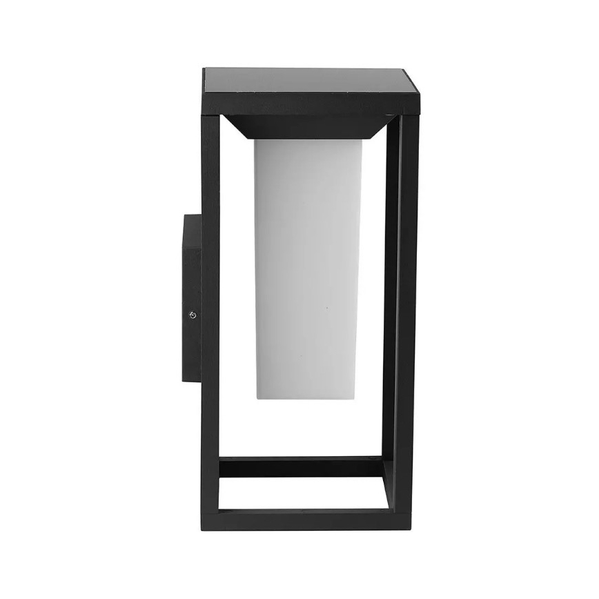 Čierna vonkajšia lampa s bielym difúzorom svieti. Je umiestnená na stene, na boku má kryt s viditeľným skrutkou.