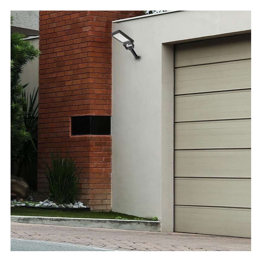 Vonkajšie nástenné LED svetlo je pripevnené k stene domu, vedľa garážových dverí. Svetlo je orientované smerom nadol. Dom má červenohnedú tehlovú stenu a svetlohnedé garážové dvere.