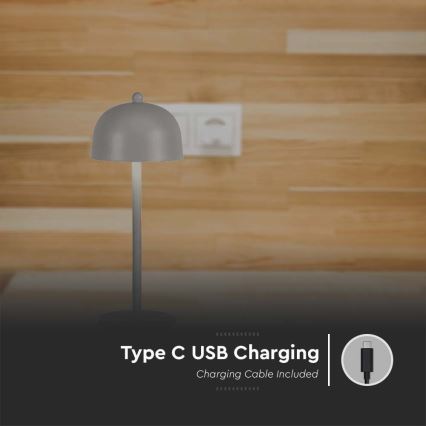 Sivá stolná lampa s kopulovitým tienidlom stojí na drevenom povrchu pred stenou. Nabíja sa cez USB-C kábel, ktorý je súčasťou balenia. Type C USB Charging, Charging Cable Included.