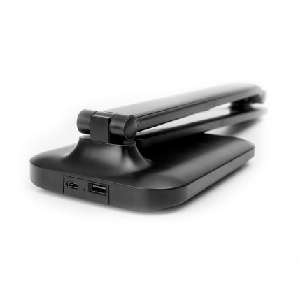 Čierna stolná lampa je zložená. Na zadnej strane základne sú viditeľné porty USB-C a USB-A. Lampa je umiestnená na bielom pozadí.