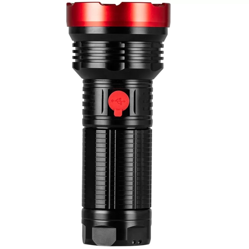 Čierna baterka s červeným vrchnákom a USB portom svieti. Baterka je valcovitého tvaru s ryhovaným povrchom. Je na bielom pozadí.