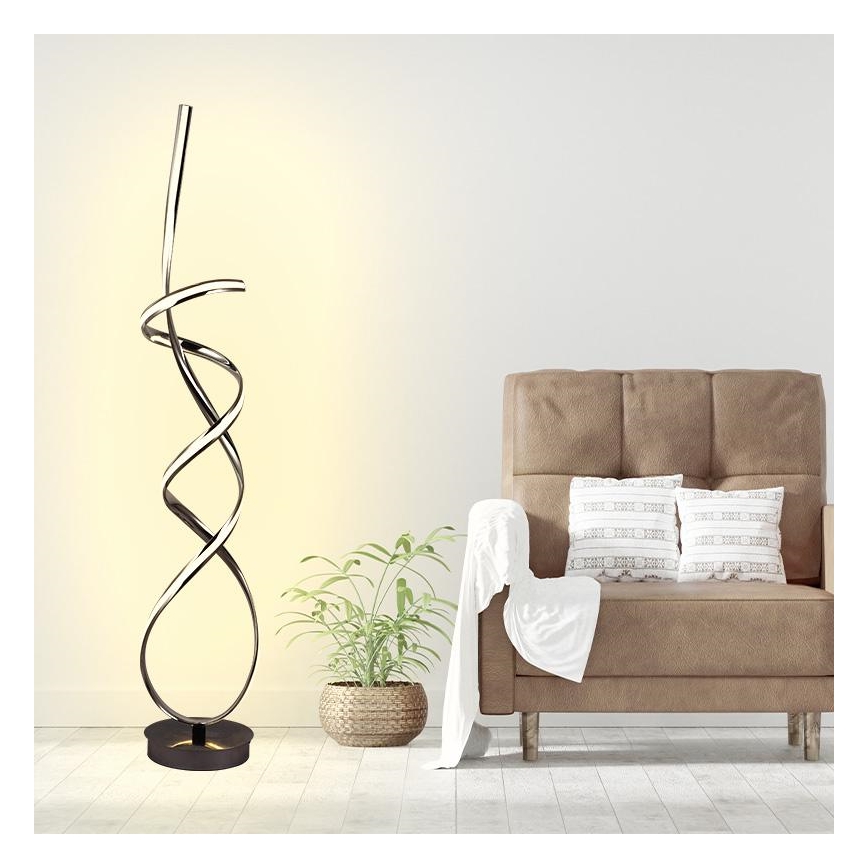 Stojacia lampa s LED osvetlením v tvare špirály svieti v obývacej izbe, blízko hnedého kresla s vankúšmi a izbových rastlín.