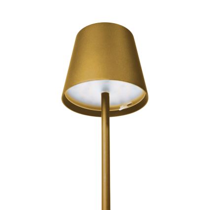 Zlatá stojacia lampa s tienidlom svieti. Stojan je vysoký a štíhly. Pozadie je biele.