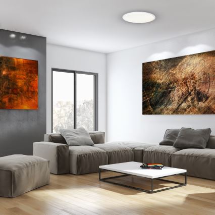 Svetlo svieti v obývacej izbe. Rohový gauč z béžovej látky je umiestnený pred konferenčným stolíkom. Na stenách visia dva obrazy.