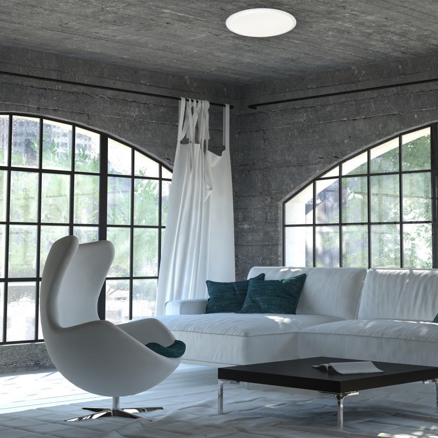 Stropné svietidlo svieti v interiéri. Biela sedačka a kreslo sú umiestnené v miestnosti s veľkými oknami a betónovými stenami.
