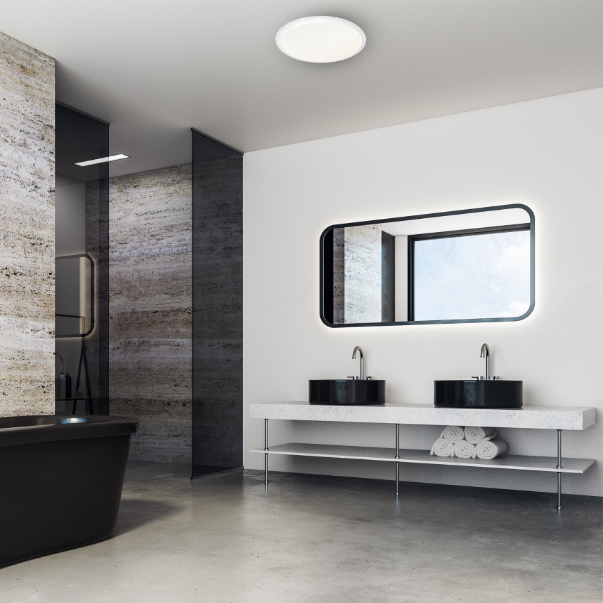 Svietidlo svieti v modernej kúpeľni. Dve čierne umývadlá sú umiestnené na minimalistickom drevenom stojane s dvoma policami, kde sú zložené uteráky. V pozadí je vidieť sprchový kút a vaňu.