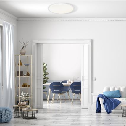 Svetlo svieti v bielom interiéri. Moderný otvorený priestor s jedálňou s modrými stoličkami a obývacou izbou s pohovkou. Na podlahe sú svetlé drevené parkety.