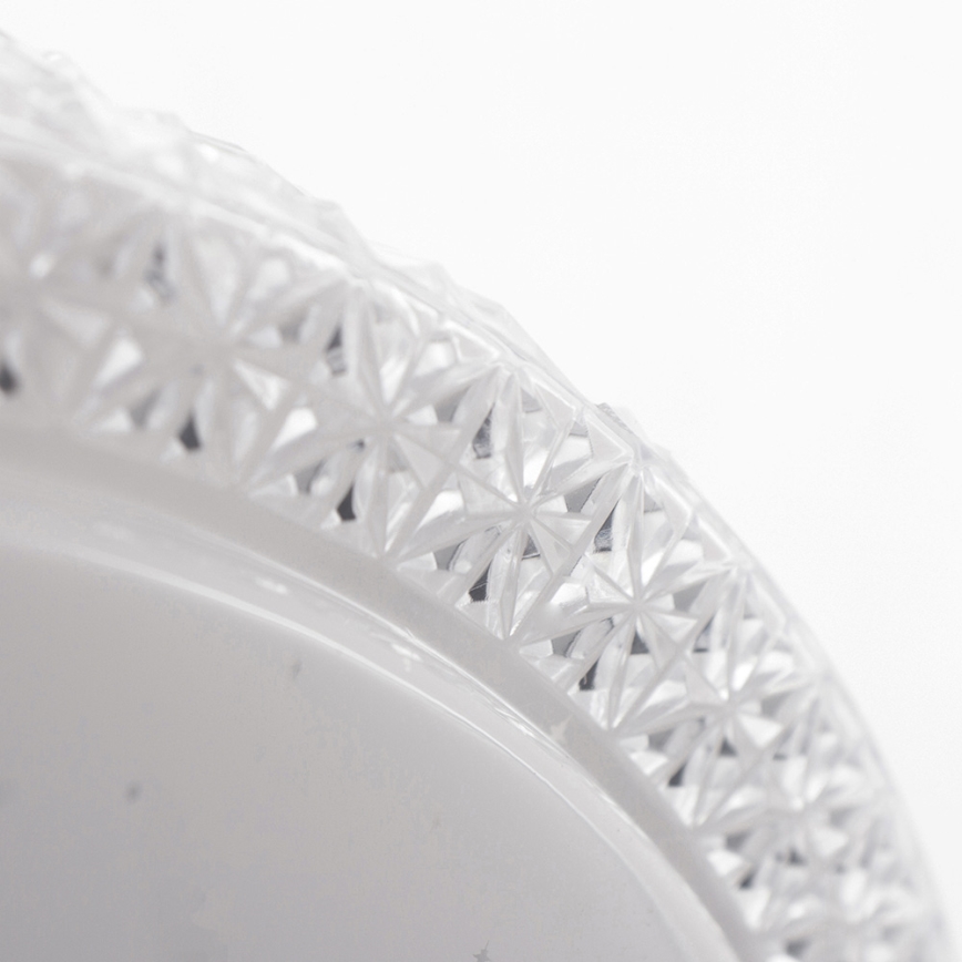 Biela miska s ozdobným okrajom. Okraj je zdobený prepracovaným geometrickým vzorom, ktorý pripomína pravidelne usporiadané kvety. Miska je snímaná zblízka pod uhlom.