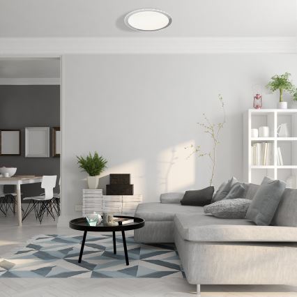 Svetlo svieti v obývacej izbe. Moderná sedačka je umiestnená pred konferenčným stolíkom. Na stenách sú rámy a polica s knihmi.