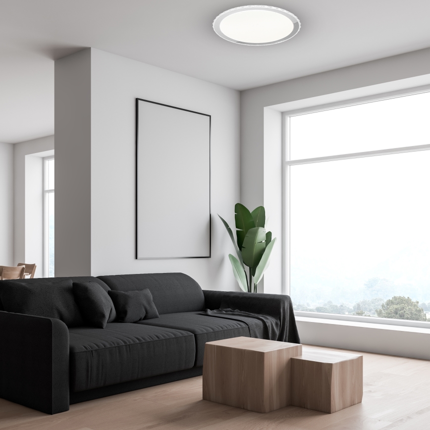 Čierna pohovka stojí v svetlej miestnosti s dreveným konferenčným stolíkom. Miestnosť má veľké okno s výhľadom na krajinu a prázdny obraz na stene.