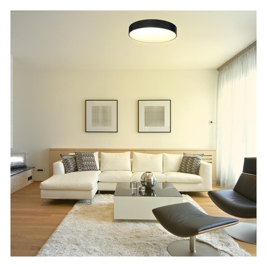 Svetlo svieti v moderne zariadenej obývacej izbe. Biela rohová sedačka je umiestnená na svetlom koberci pred bielym konferenčným stolíkom. V pozadí sú dva obrázky a tmavé kožené kreslo.