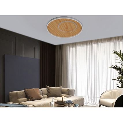 Svietidlo je pripevnené k stropu. Má okrúhly tvar, drevenú vložku a biely okraj. Nachádza sa v obývacej izbe s pohovkou, konferenčným stolíkom a závesmi.