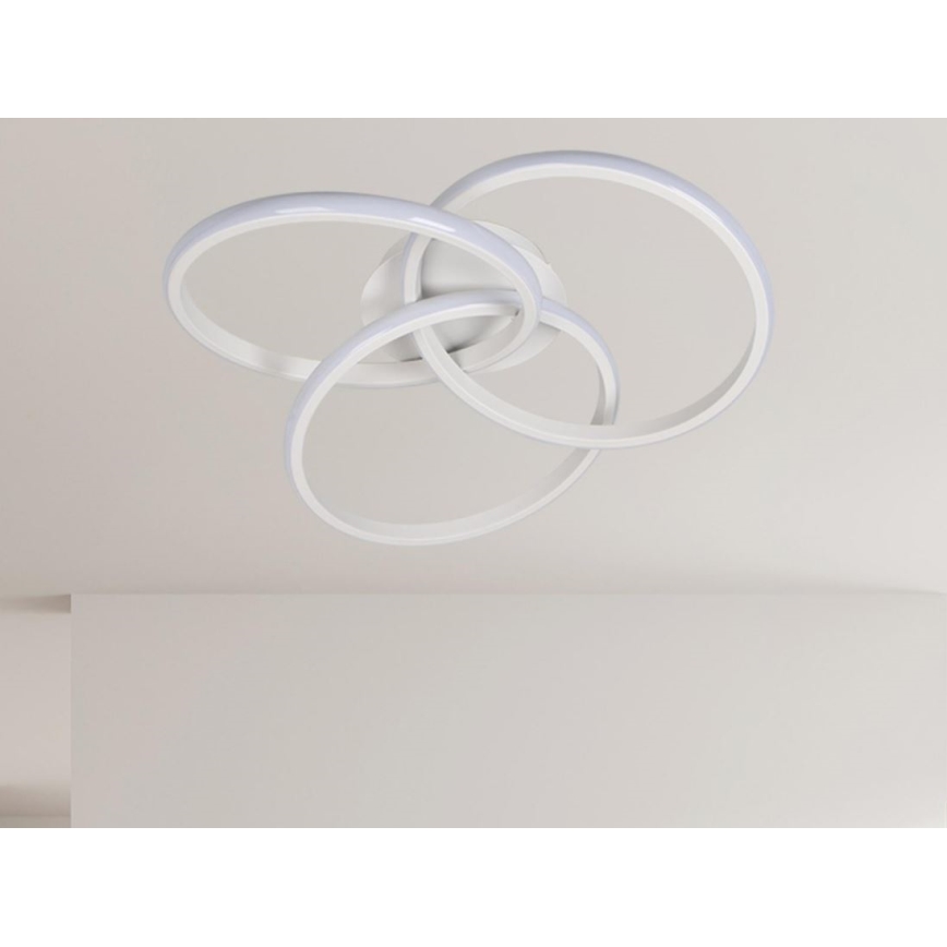 Svietidlo s prepletenými bielymi kruhmi je pripevnené na svetlom strope. Kruhy sú osvetlené vnútorným svetlom. Svietidlo je v interiéri.