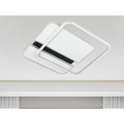 Nástenná lampa s dvoma prekrývajúcimi sa štvorcovými bielymi prvkami a čiernym detailom, visí z bieleho stropu nad bielou poličkou.