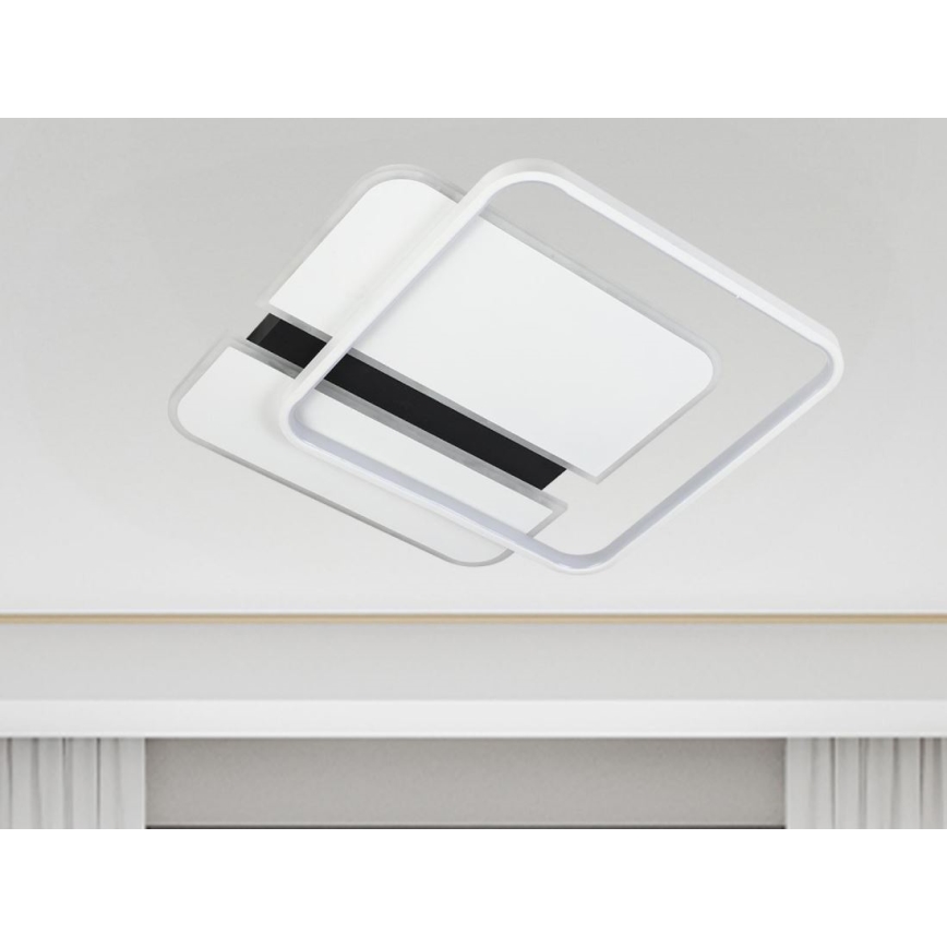 Nástenná lampa s dvoma prekrývajúcimi sa štvorcovými bielymi prvkami a čiernym detailom, visí z bieleho stropu nad bielou poličkou.