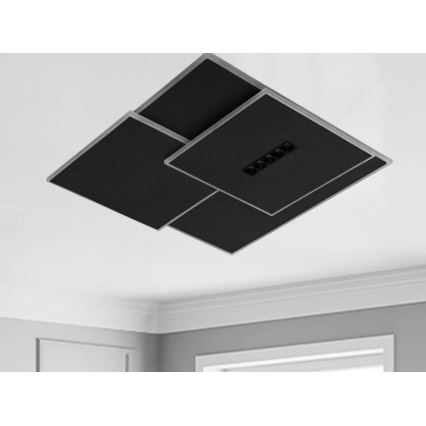 Čierne štvorcové svietidlo s integrovanými svetlami je pripevnené k stropu. Svietidlo je zložené z prekrývajúcich sa panelov s tenkým strieborným rámom. Je umiestnené v interiéri miestnosti s bielym stropom a svetlosivými stenami.