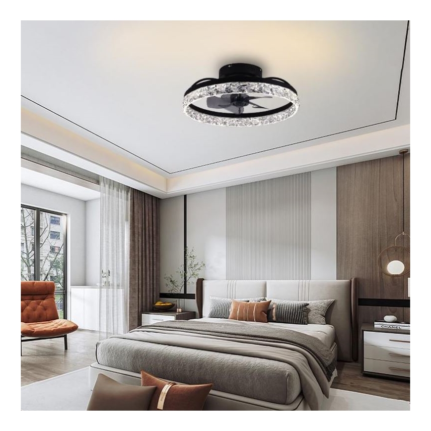 Stropný ventilátor s LED osvetlením je umiestnený v spálni. Ventilátor je čierny s kryštálmi. V pozadí je posteľ a kreslo.