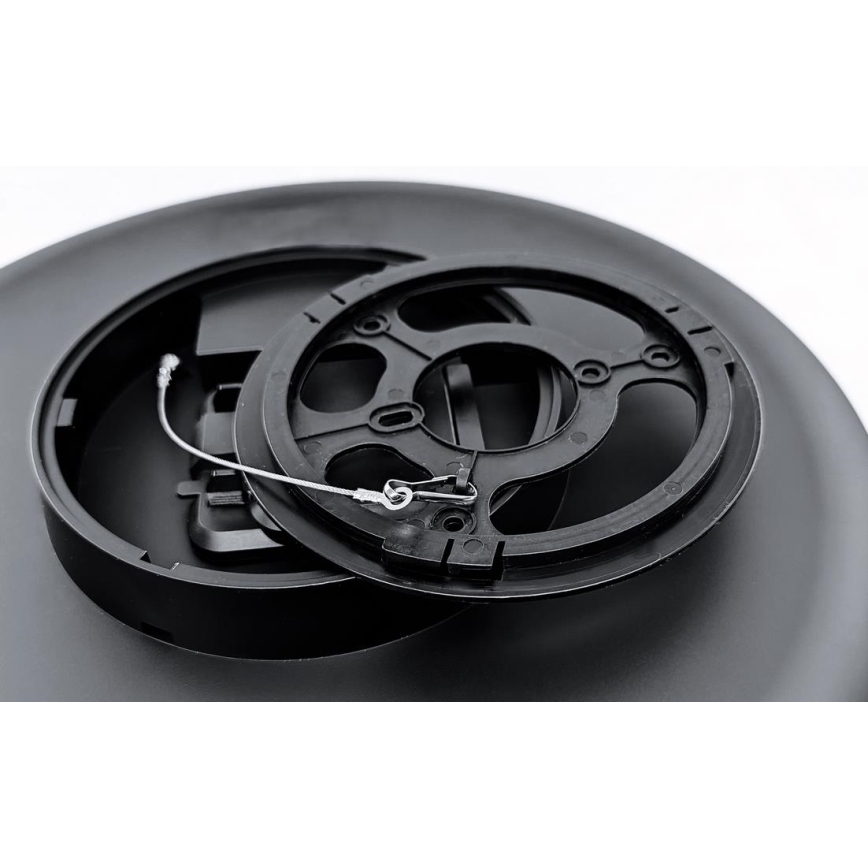 Dve čierne plastové kruhové súčiastky sú rozložené, menšia je položená na väčšej. Medzi nimi je pripevnený tenký kovový lankový drôt. Sú na svetlom pozadí.