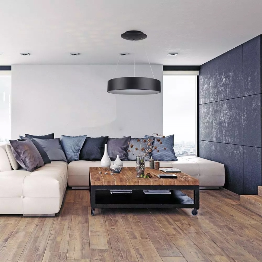 Moderná obývacia izba s rohovou sedačkou a dreveným konferenčným stolíkom. Nad stolíkom visí kruhové stropné svietidlo. Priestor je doplnený tmavou stenou.